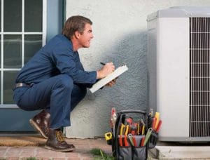 A man kneeling down next to an air conditioning unit.