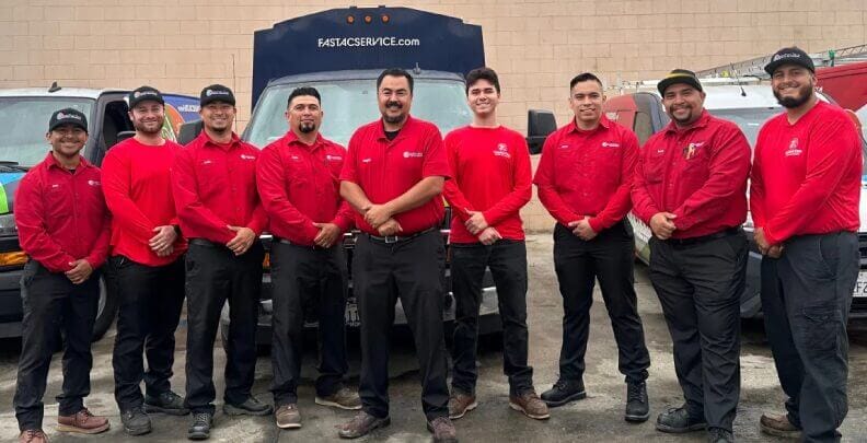 A team of technicians in red uniforms, specializing in heating and cooling systems, smiling and standing together outside their workplace.