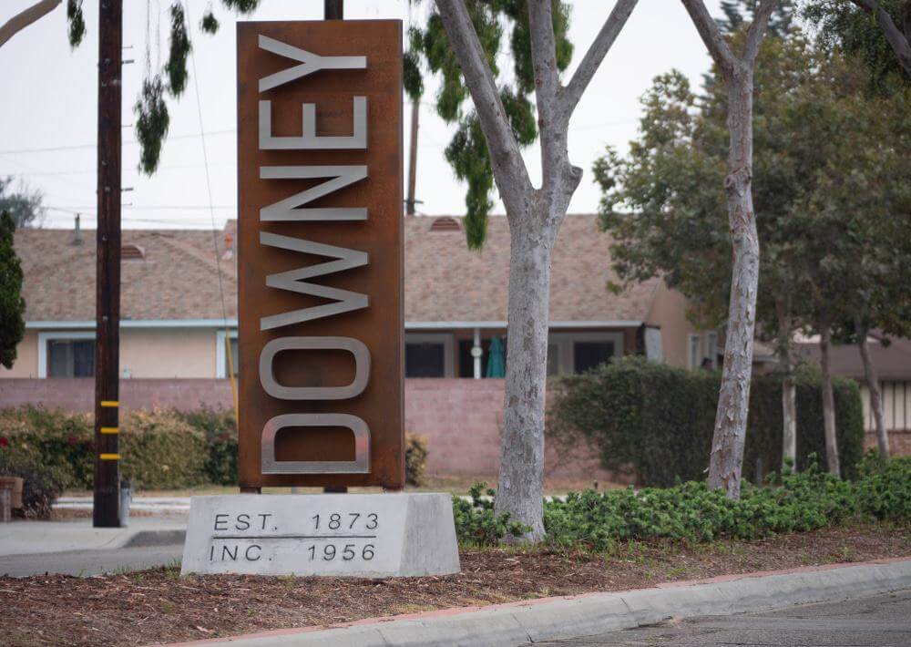 A large sign reading "downey" with "est. 1873 inc. 1956" beneath it, set against a background of trees and a building.